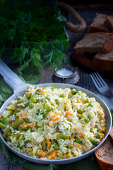 Rice with vegetables - carrots, onions, broccoli, pepper, green peas in a frying pan on a wooden table, selective focus