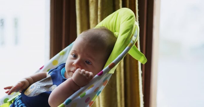 Little baby in bouncy chair by the window at home