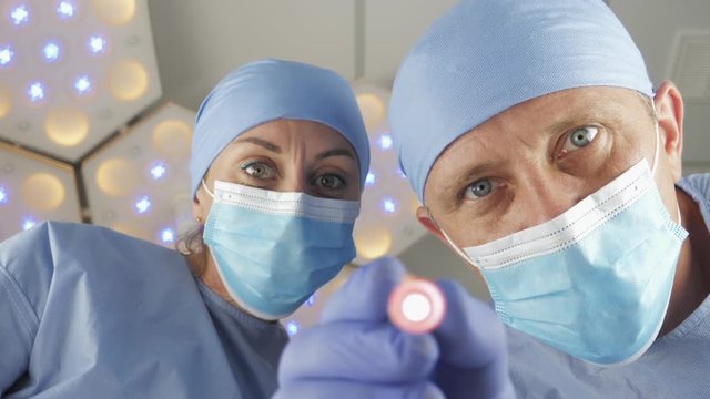 Doctor surgeon with assistant checks the reaction of the pupils of the eyes with bright light. The patient wakes up after a coma. First-person view