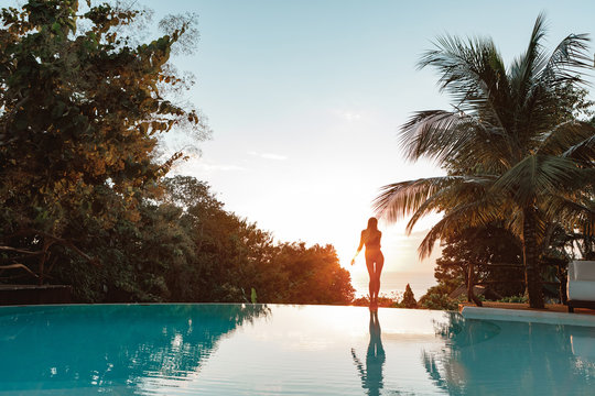 Girl stand  on edge of infinity pool at beautiful sunset amazing tropical jungle  and sea view