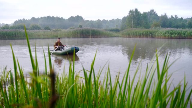 young stylish hipster fisherman sails in a boat on a lake or river between the reeds. A young man paddles on an inflatable boat. Relaxes in nature. camping by the water. Recreation