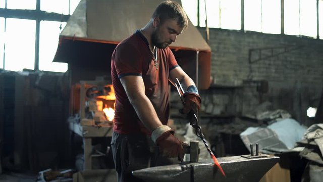a blacksmith uses a hand hammer on an anvil to forge a red hot metal product