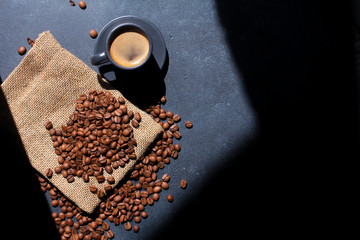 Espresso cup and coffee beans on sackcloth on dark background with geometrical shadow. Roasted grains, copy space, top view. Coffee shop, caffeine, morning concept