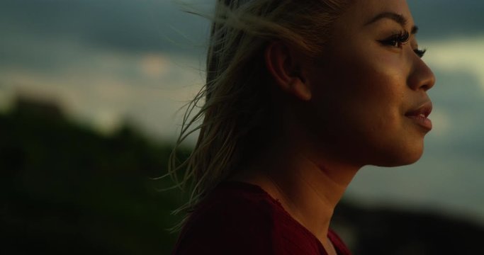 Portrait of woman in profile looking out at ocean at sunset as wind blows through her hair while on vacation. Travel, holidays, 4K