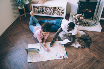 Multiracial couple doing travel marks on map lying on floor