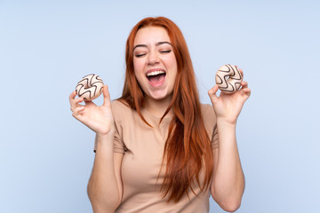Redhead teenager girl over isolated blue background holding donuts with happy expression