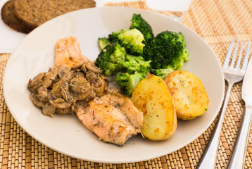 fried river trout fillet with a complex side dish of broccoli, baked potatoes and mushroom sauce