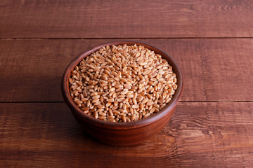 Wheat grains in clay bowl on brown wooden table. Top view, high angle, closeup. Harvest, healthy food, ingredient concept
