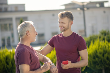 Bearded male with smartphone patting mature man with smartwatch on shoulder