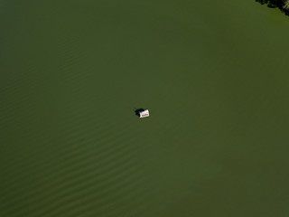 Fishing boat on green water, aerial drone view. Algae bloom in the river, green pattern on the water.