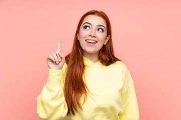 Redhead teenager girl over isolated pink background intending to realizes the solution while lifting a finger up
