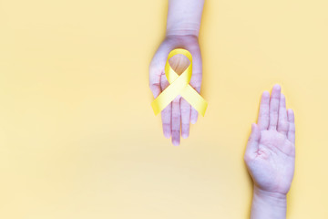 Human hands giving yellow gold ribbon awareness symbol for support suicide prevention,...