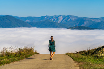 Behind a beautiful woman barefoot and dressed in an elegant green dress that observes and admires the landscape on a high road leading to the distant mountains covered with fog during a sunny morning