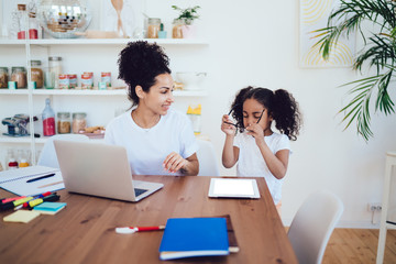 Curly little daughter with smiling freelance mother at home