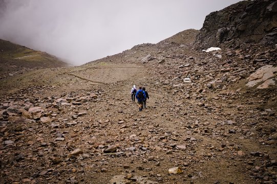 Three people are climbing a mountain on a foggy day on the italian Alps (Peio, Trentino - Alto Adige, Italy, Europe)