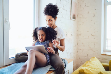 Disgusted daughter using tablet with mother near window