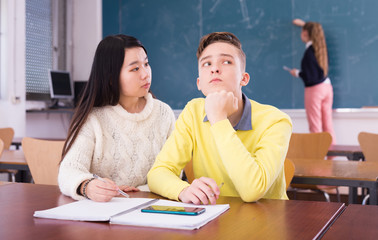 Young guy and chinese girl students doing lesson in classroom, female student writing on whiteboard