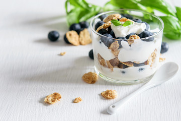 Granola with blueberries and yogurt, green leaves of basil on the white rustic table. Healthy fitness food.