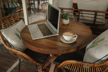 Open laptop on round wooden table with cup of coffee in cafe, working place in cafe terrace