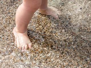 Small baby feet close-up on the sand of the sea beach. Sea water washes the feet. Happy childhood. Rest at the sea. Summer sunny day. Copy space.