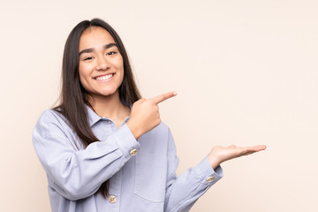 Young Indian woman isolated on beige background holding copyspace imaginary on the palm to insert...