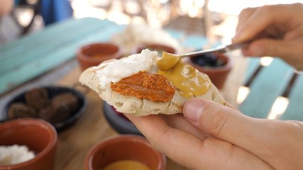 Meze for breakfast. Hand spreading different dips on freshly baked pita with knife. Healthy organic vegan middle Eastern cuisine.