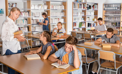 Upset boy and girl sitting with books during lesson, teacher helping them in the classroom