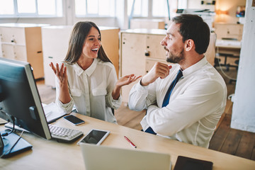 Cheerful male and female business partners enjoying live communication during break form work, successful professional man and woman dressed in formal wear talking while cooperating in office desktop