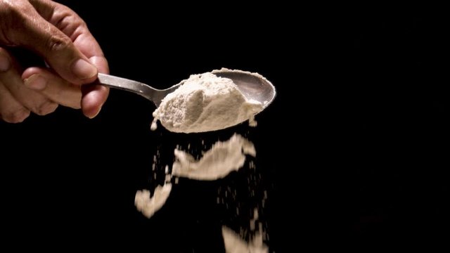 Flour being poured off a tablespoon super slow motion on a black backdrop