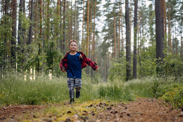 Fototapeta na wymiar Cute boy with happy smiling face wearing plaid flannel shirt running down the lane in the forest