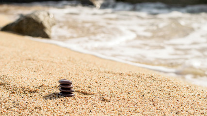 Small natural stones piramid on the sand. Sea side blurred background.