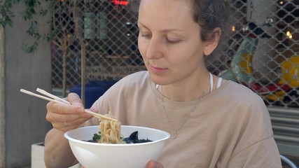 Healthy vegan Asian cuisine. Hungry Caucasian girl eating vegan ramen soup with a big pleasure. 