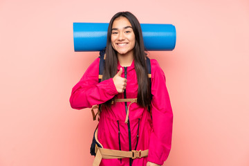Young mountaineer Indian girl with a big backpack isolated on pink background giving a thumbs up gesture
