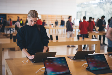 Young female customer standing near table with electronic products while examining the goods, store...