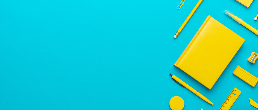 Top view photo of yellow stationery over turquoise blue background with copy space. Flat lay image of stickers, pencils, notebook, ball-point pen, eraser, sharpener, paerclips, pushpins and ruler.