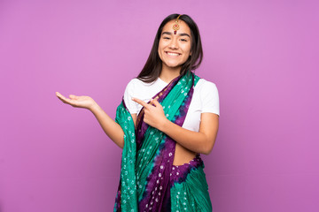 Young Indian woman with sari over isolated background holding copyspace imaginary on the palm to...