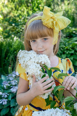 beautiful little girl with long Golden hair, white flowers and a yellow bow looks at the camera with a smile