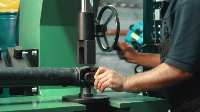 Car cardan shaft repair. A locksmith dismantles a faulty gimbal part using a mechanical press in a workshop. Close-up.