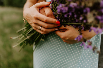 Fototapeta premium holding a bouquet of lilac purple flowers. A woman has a wedding ring on her finger. The girl is dressed in a turquoise dress with peas. Hands of people in love close up.