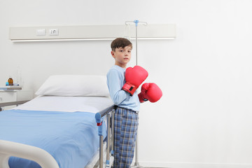 Child in hospital room with boxing gloves fighting his disease isolated on white wall with copy space