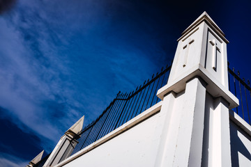 High white concrete walls with metal bars separate the dead from an outside cemetery, background with a blue sky.