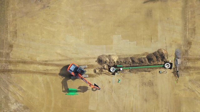 Tiefbau, Kanalbau, Leitungsbau auf einer Baustelle: Bagger verlegt Rohr, Vogelperspektive