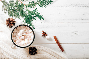 Obraz na płótnie Canvas cocoa mug with marshmallows, white sweater, fir branches , cones, cinnamon sticks, star anise on a white wooden background, hot winter drink, copy space