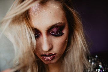 Pensive woman with shiny purple makeup looking down. Closeup portrait of magnificent european girl with long black eyelashes.