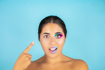 Beauty portrait of female model with vivid makeup on one half of the face and clean face on the other part on blue background and blue lips.