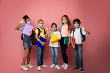 Obraz premium Education during virus pandemic. Full length portrait of schoolkids in medical masks waving on pink background
