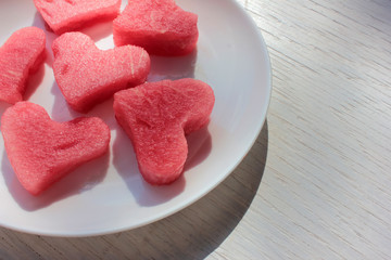 Plakat Watermelon slices in the heart shape on a white plate on wooden table. Top view, copy space. 