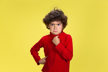 Pointing at himself. Portrait of pretty young curly boy in red wear on yellow studio background. Childhood, expression, education, fun concept. Preschooler with bright facial expression and sincere