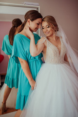 stylish happy bride dressing in dress, smiling to bridesmaids, at window, rustic wedding morning preparation. bridal getting ready. emotional moment. space for text. black white photo