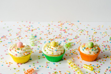 Three brightly colored homemade cupcakes on a white wooden background with sprinkles
